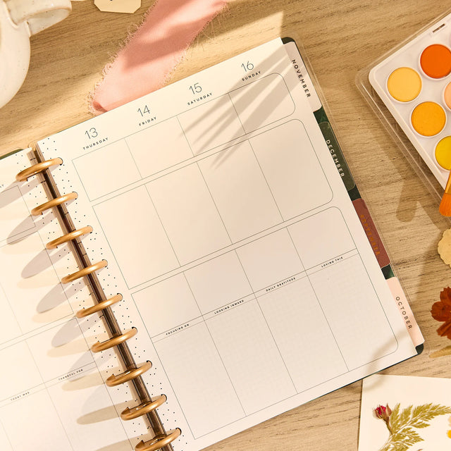 Planner on a wooden surface with watercolor paint set and leaves