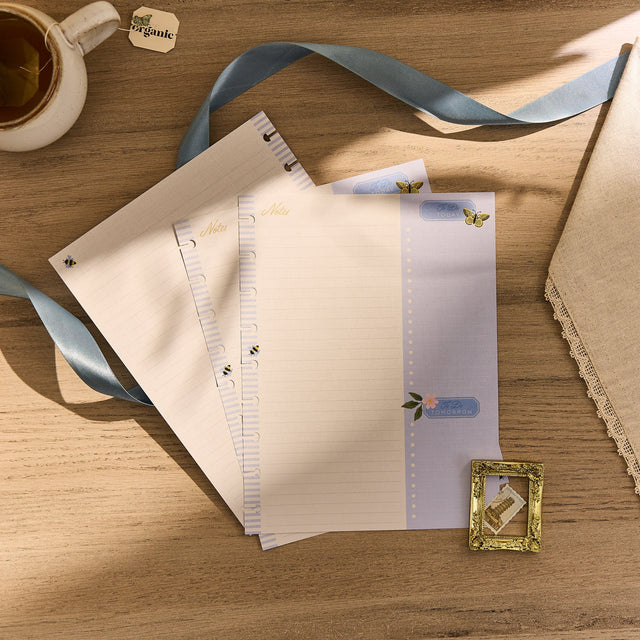 Set of stationery items including paper, a ribbon, and a cup on a wooden surface.