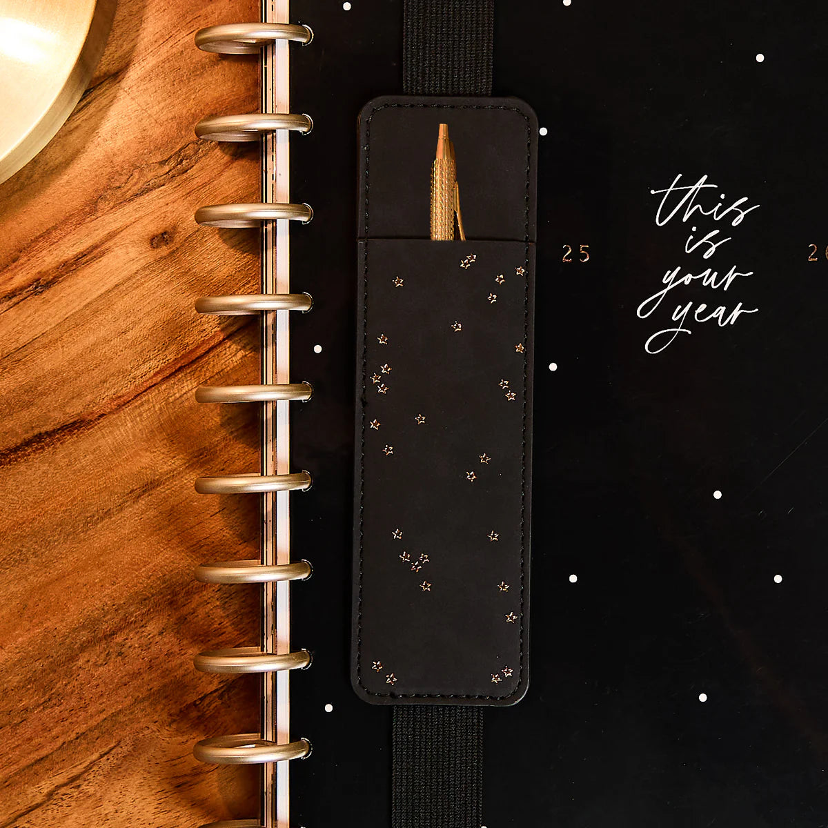 Happy Planner Dainty Neutrals Vegan Leather Slim Pen Holder Black leather planner charm with gold accent on a wooden planner against a black background with 'this is your year' text.