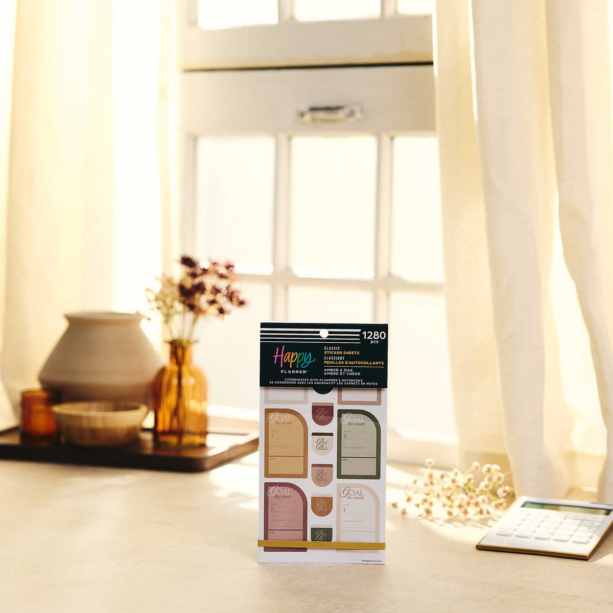 Happy Planner Amber & Oak Budget sticker book displayed near a sunlit window and calculator