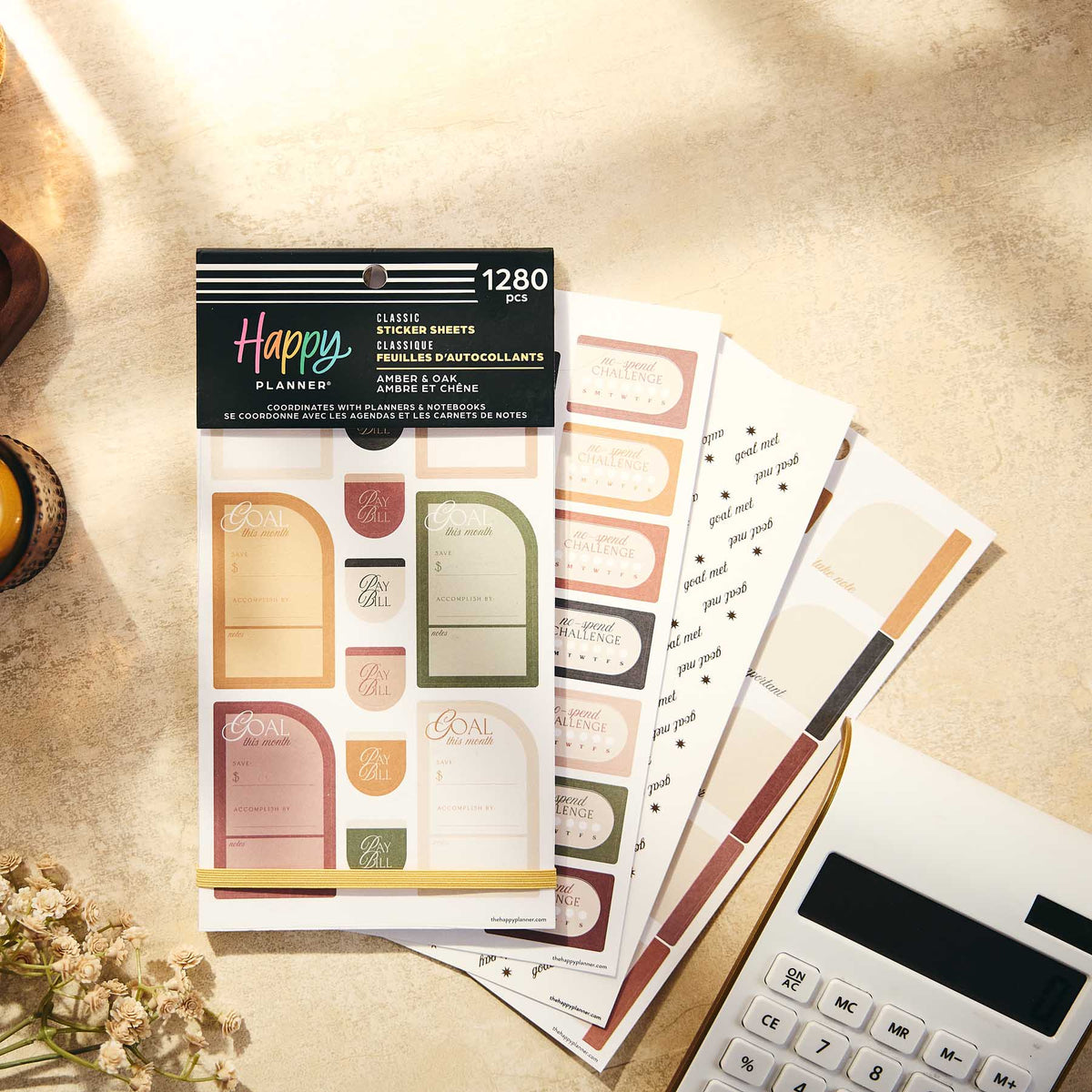 Amber & Oak Budget sticker book and savings labels beside a calculator on a sunlit tabletop