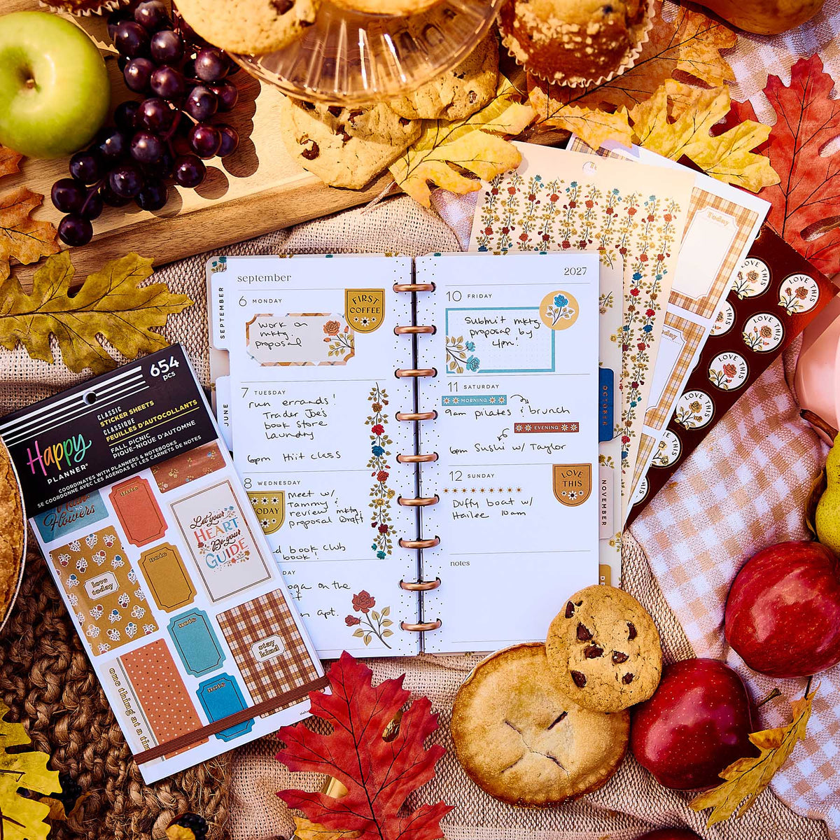Open disc-bound planner decorated with Fall Picnic stickers beside the sticker book, apples, grapes and cookies