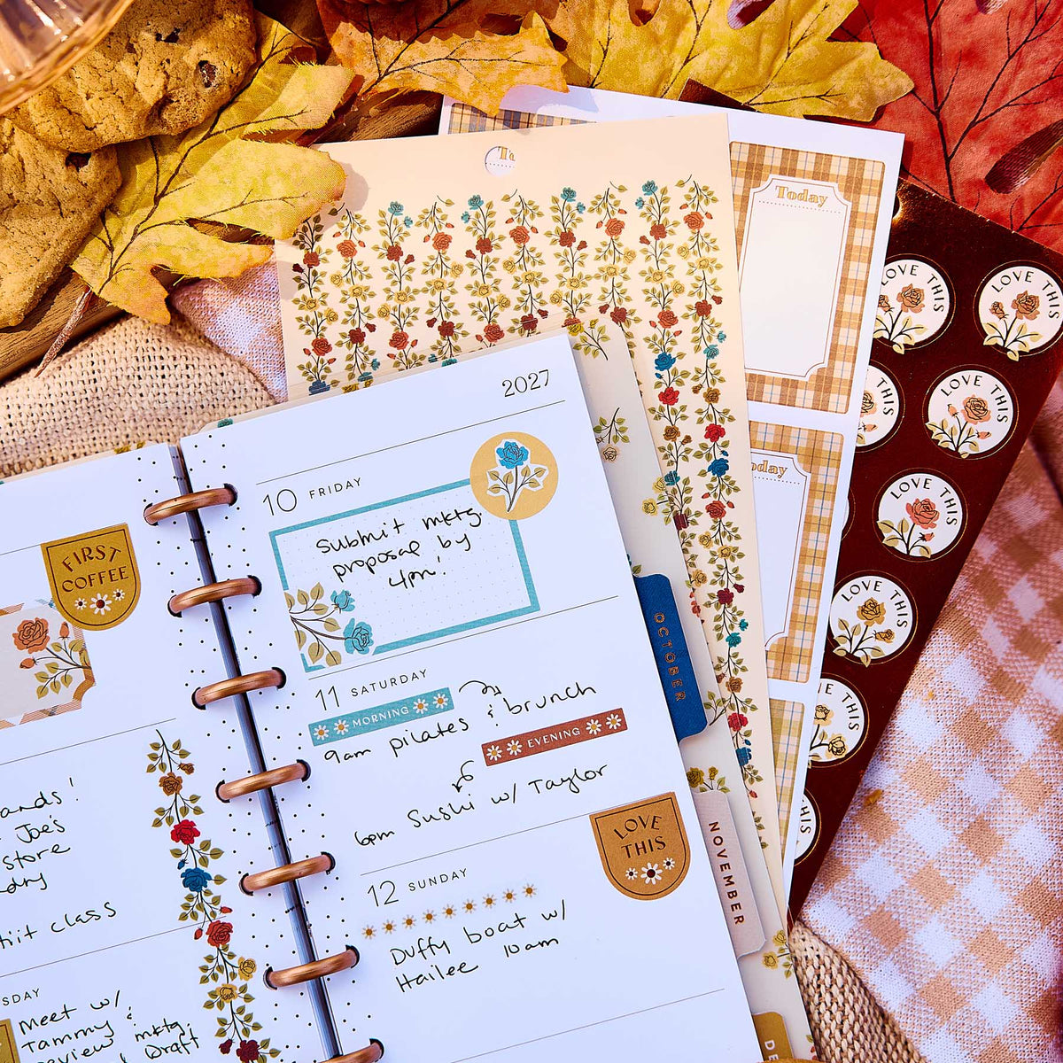 Close-up of a weekly planner decorated with Fall Picnic boxes and florals beside sticker sheets and autumn leaves