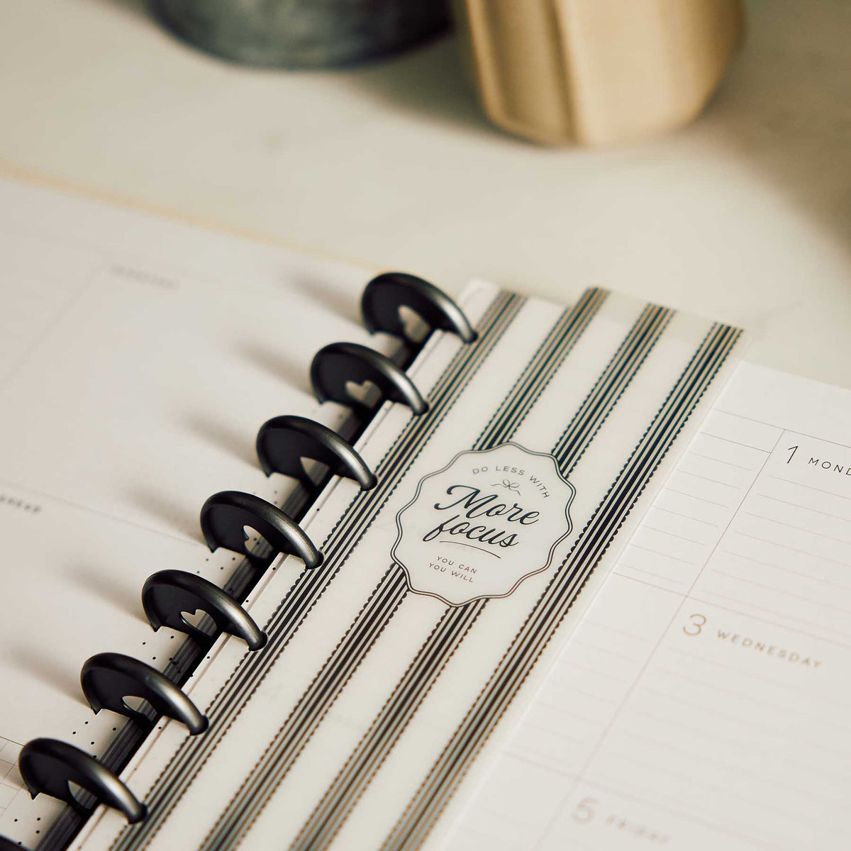 Close-up of the striped Modern Balance bookmark with More Focus wording attached to black planner discs