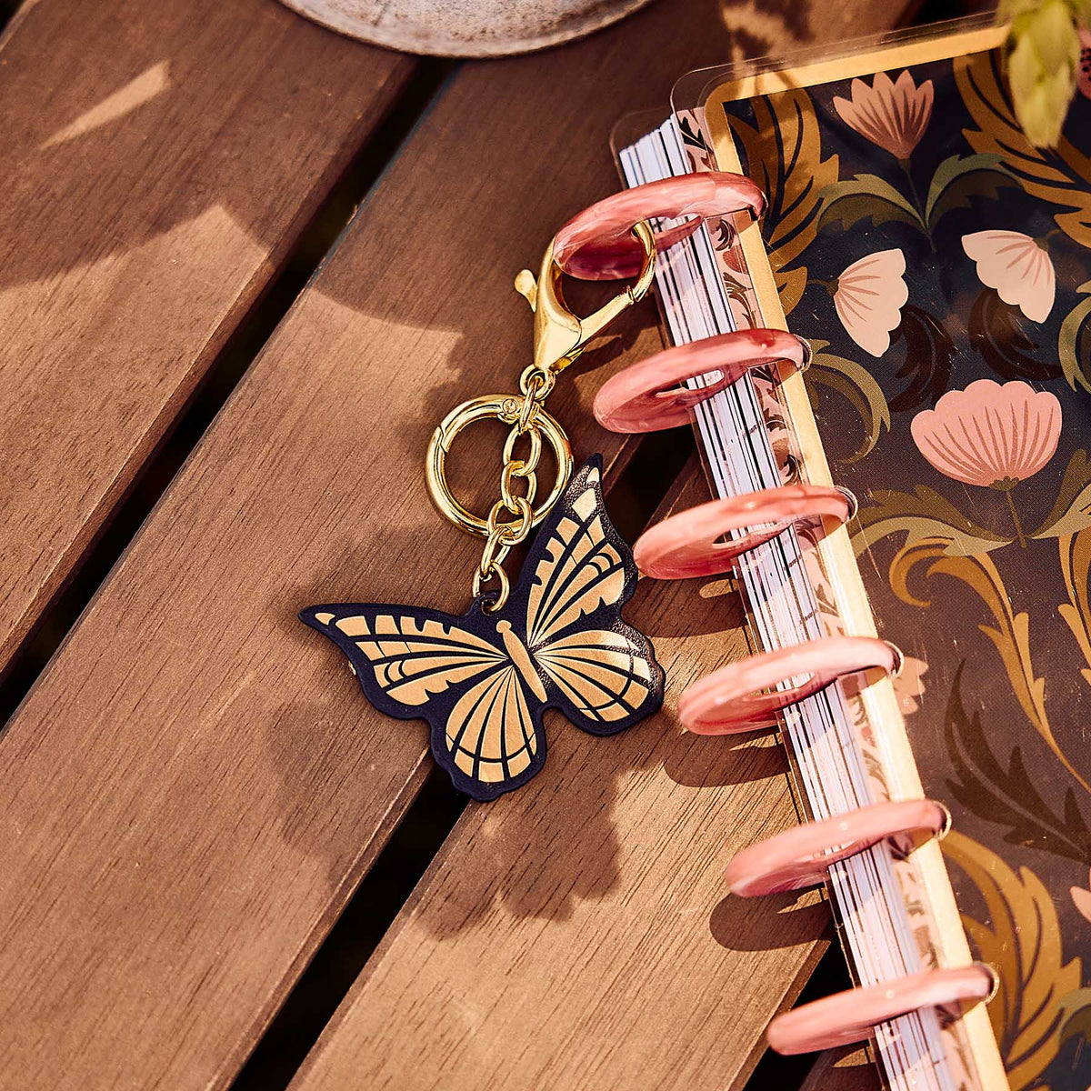 Butterfly Planner Charm hanging from a pink disc on a floral Happy Planner