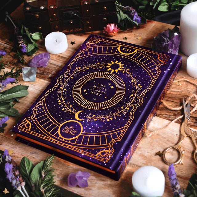 Purple book with gold designs on a wooden surface with candles and crystals