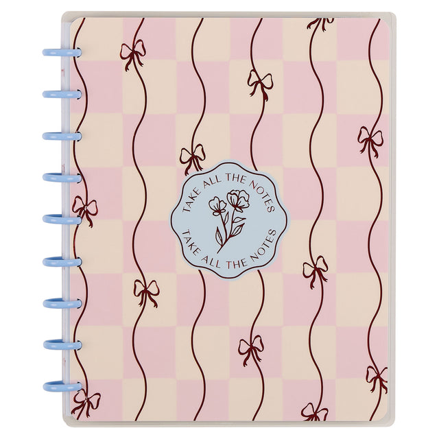 Notebook with decorative cover featuring ribbons and a logo on a pink and beige checkered background.