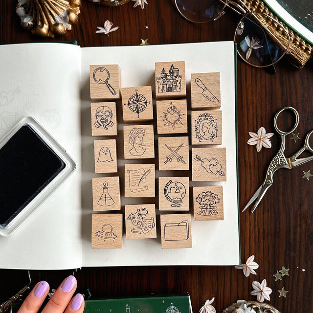 Book Genre Stamp Set on white paper with an ink pad and scissors on a wooden surface.