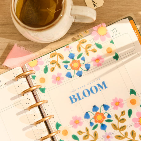 Floral-themed planner with a cup of tea on a wooden surface featuring the Happy Planner Golden Garden Classic Dashboard Pack