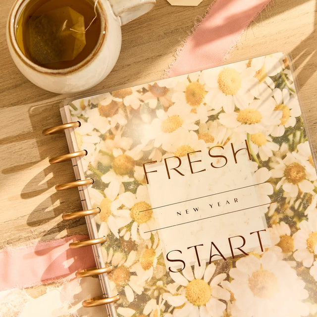 Floral wellness planner with 'Fresh New Year Start' text next to a cup of tea on a wooden surface.