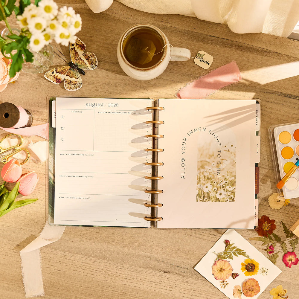 Open planner on a wooden table with flowers, tea, and stationery items.