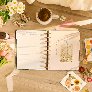 Open planner on a wooden table with flowers, tea, and stationery items.