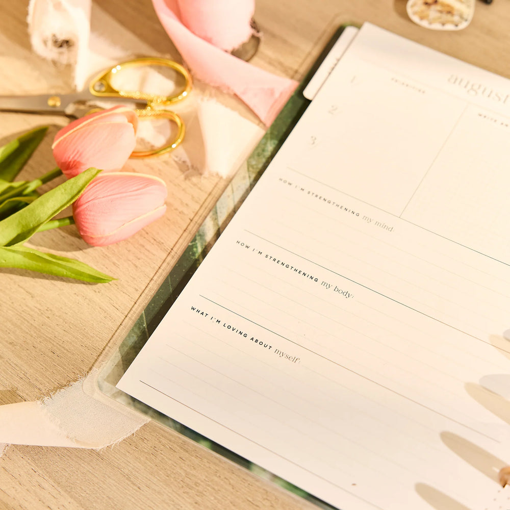 Happy Planner 2026 - 2027 Modern Nature Wellness Classic 12 Month Dated planner with a pen on a wooden surface with pink tulips and scissors.