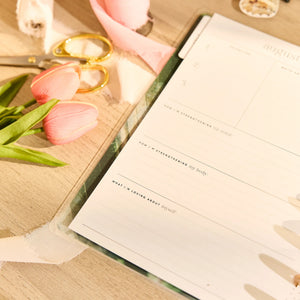Happy Planner 2026 - 2027 Modern Nature Wellness Classic 12 Month Dated planner with a pen on a wooden surface with pink tulips and scissors.