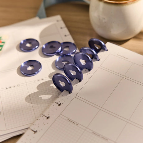 Happy Planner Forget Me Not Heart Metal Disc Set on an open notebook with a blurred background