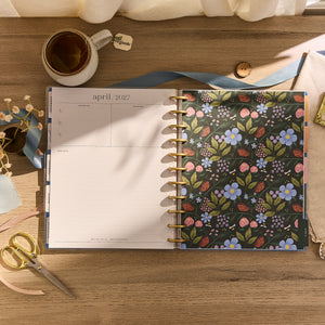 Floral-patterned planner on a wooden surface with a cup and scissors.