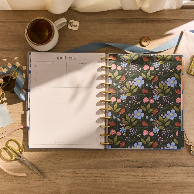 Floral-patterned planner on a wooden surface with a cup and scissors.