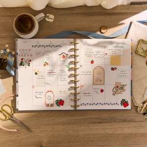 Open planner with decorative pages on a wooden desk with a cup and stationery items.