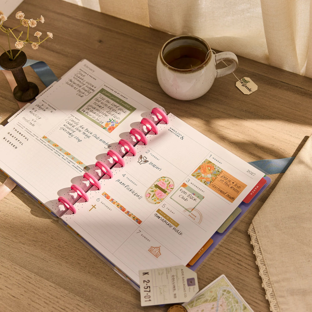 Open Happy Planner 2026 - 2027 French Papers Faith Classic 12 Month Dated planner on a wooden table with a cup of tea and decorative elements.
