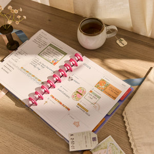 Open Happy Planner 2026 - 2027 French Papers Faith Classic 12 Month Dated planner on a wooden table with a cup of tea and decorative elements.