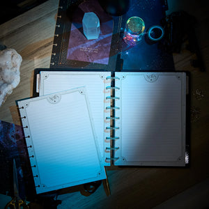 Open planner with lined pages on a wooden surface with crystals and cards.