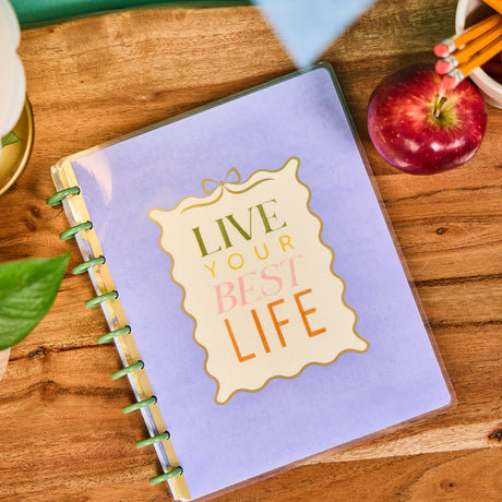 Happy Planner Fruit Stand Classic Notebook with 'Live Your Best Life' quote on a wooden table with an apple and pencils.