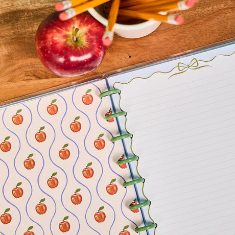 Notebook with apple pattern, red apple, and pencils on a wooden surface