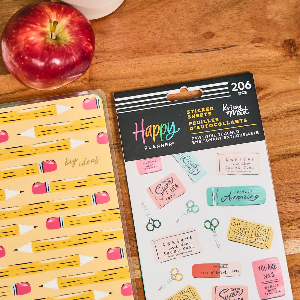 Happy Planner sticker sheet with decorative stickers on a wooden surface next to an apple.