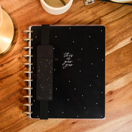 Black pen holder with star patterns on a planner with a wooden surface background