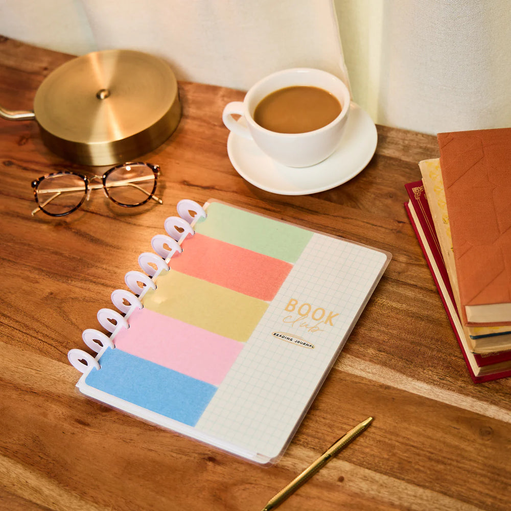 Colorful planner on a wooden desk with a cup of coffee, glasses, and books.