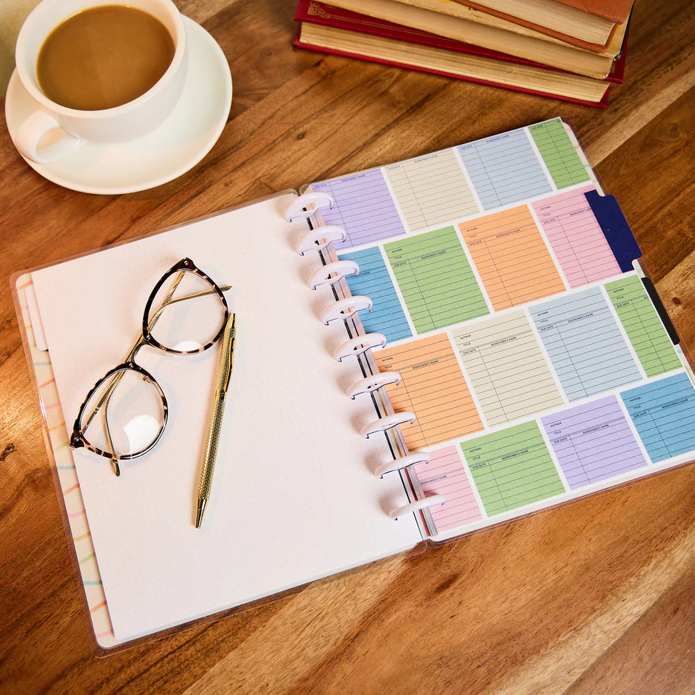 Colourful journal on a wooden table with a cup of coffee and glasses.