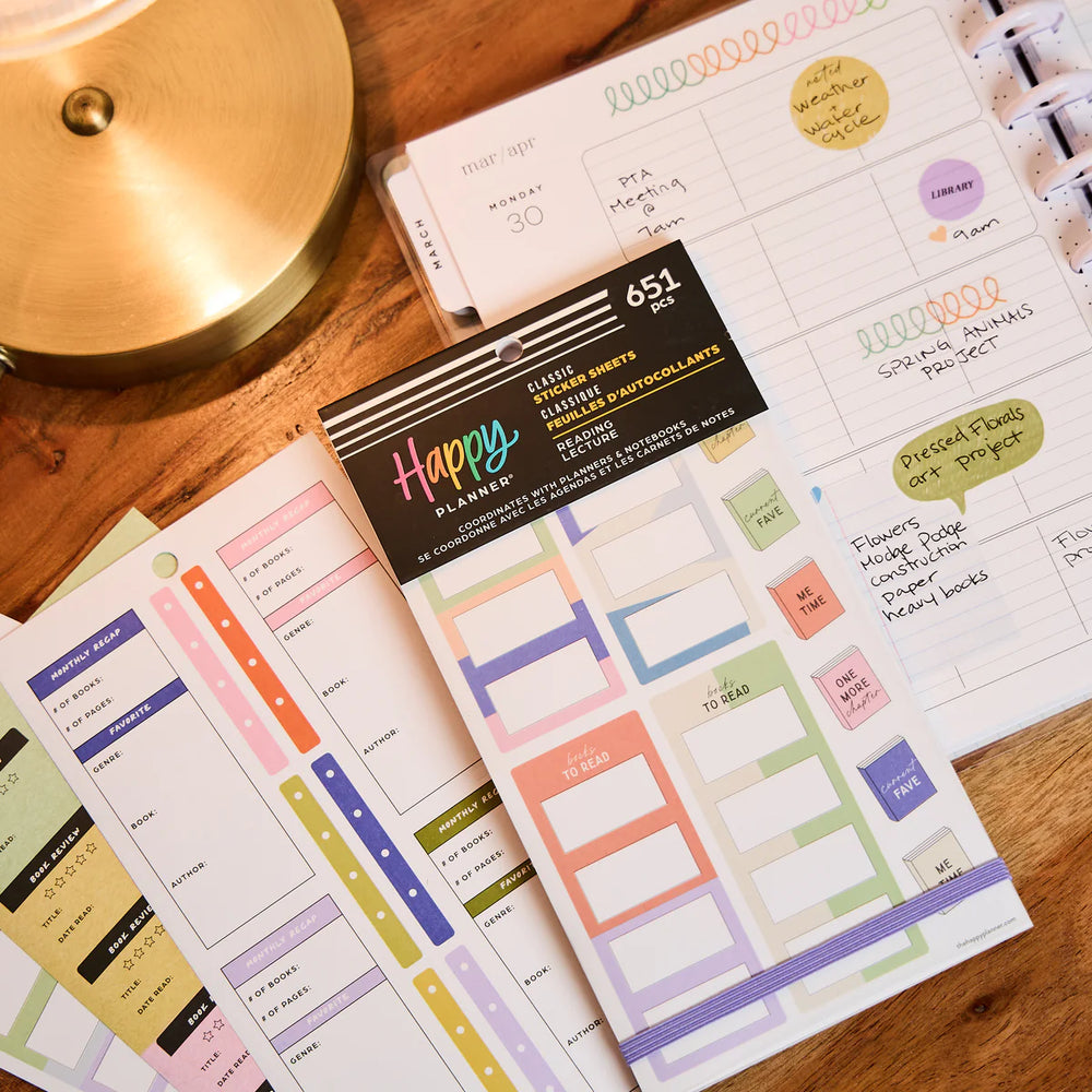 Happy Planner stickers on a wooden surface with a lamp in the background