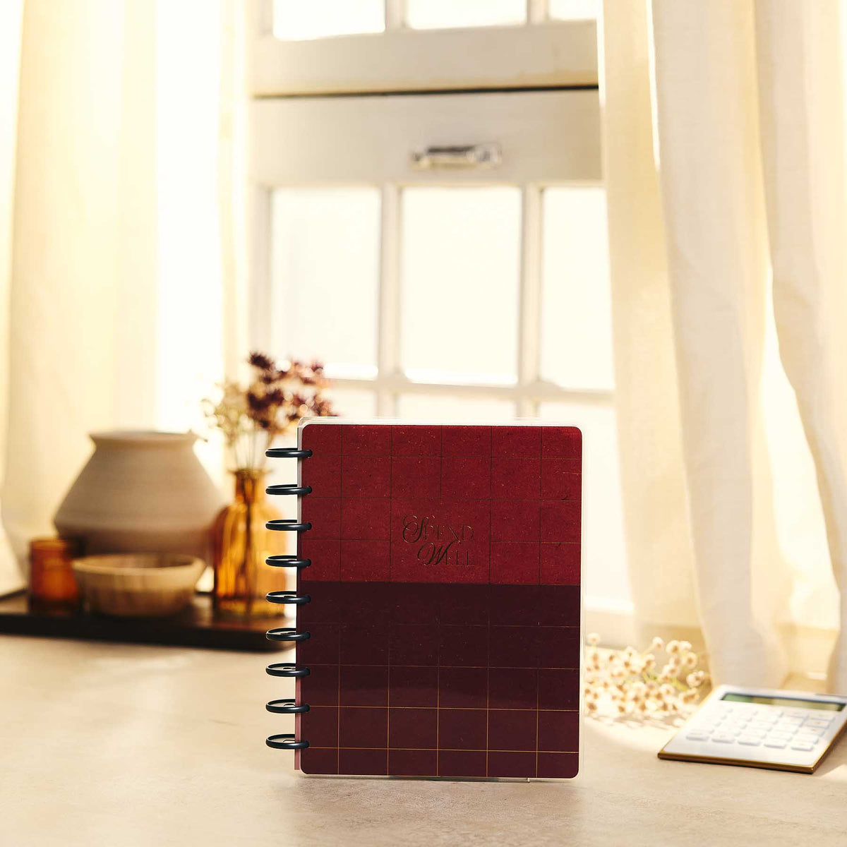 Amber & Oak red disc-bound budget journal on a kitchen counter beside a calculator