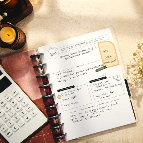 Open Amber & Oak journal with handwritten budget prompts beside a calculator and candle