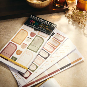 Amber & Oak Budget sticker book with planning sheets in earthy colours arranged on a tabletop