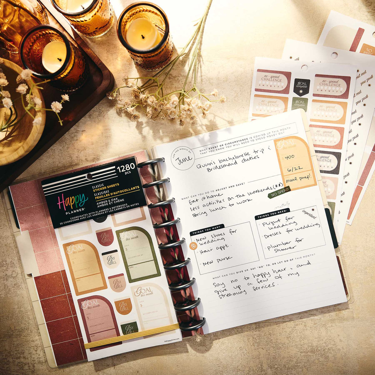 Amber & Oak Budget sticker book and bill labels beside a disc-bound planner and lit candles