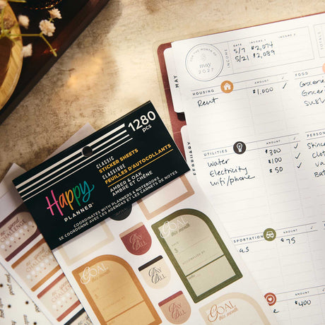 Close-up of Amber & Oak Budget sticker book beside a handwritten budget and savings goal page