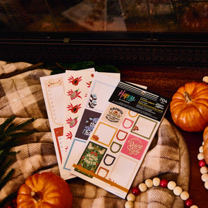 Bright Seasons sticker book and floral sheets on a checked blanket beside pumpkins and a fireplace