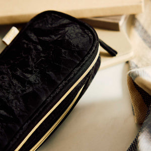 Onyx black textured pouch beside a notebook and woven textile