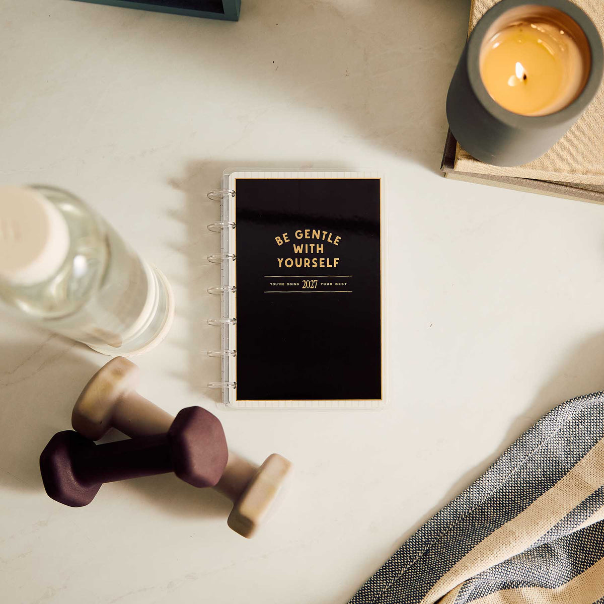 Haven and Heart black fitness planner beside dumbbells, water bottle, candle and notebook