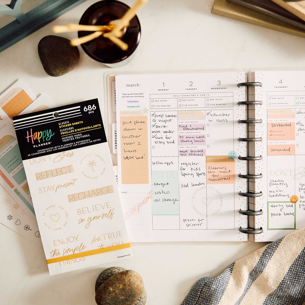 Happy Planner Hushed Hues sticker book beside an open weekly spread with handwritten plans and pastel boxes