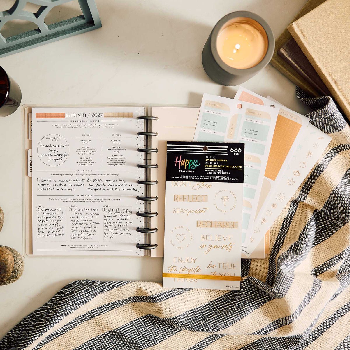 Hushed Hues sticker book and reflection stickers beside an open planner, candle and striped fabric