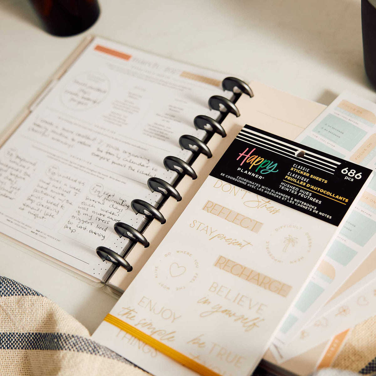 Happy Planner Hushed Hues sticker book beside a disc-bound planner with handwritten wellness notes