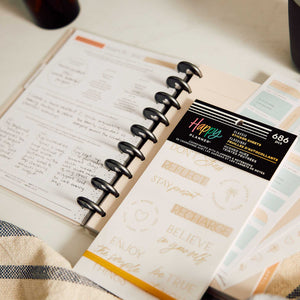 Happy Planner Hushed Hues sticker book beside a disc-bound planner with handwritten wellness notes