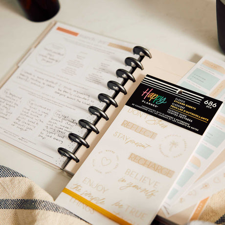 Happy Planner Hushed Hues sticker book beside a disc-bound planner with handwritten wellness notes