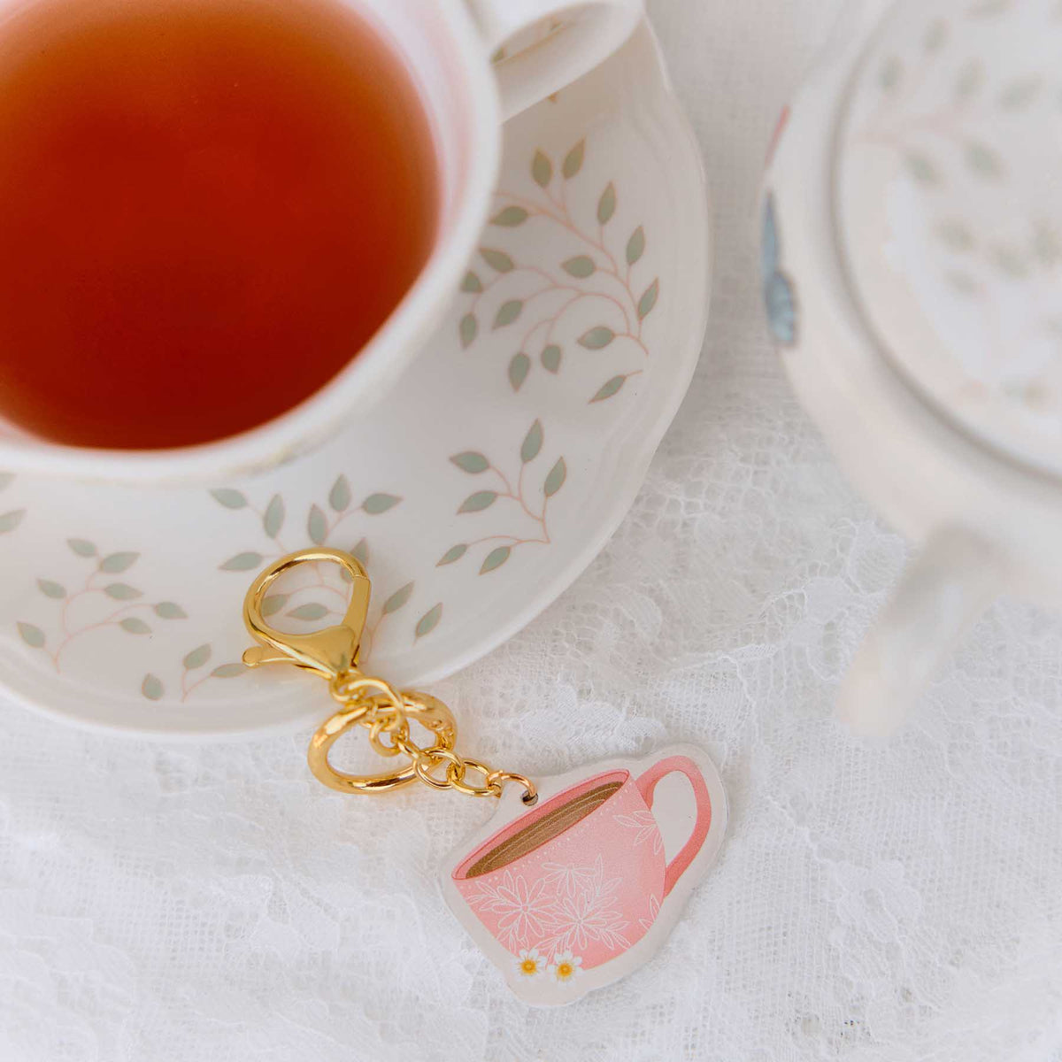 Pink Coffee Planner Charm beside a floral teacup and saucer on white lace