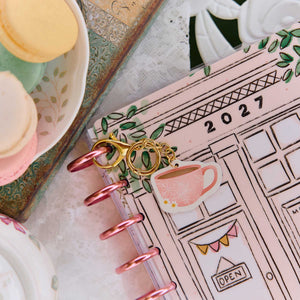 Happy Planner Coffee Planner Charm clipped to pink discs on an illustrated planner