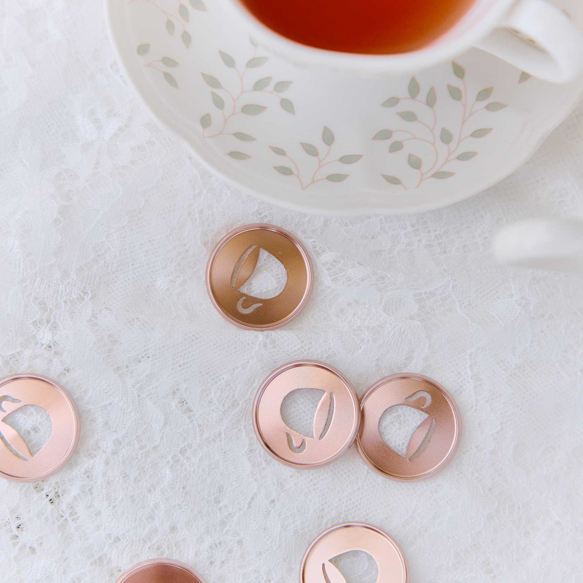 Latte coffee cup discs beside a floral coffee cup on lace fabric