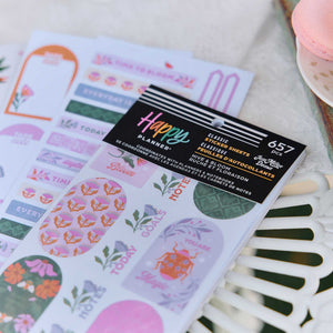 Close-up of Hive & Bloom sticker book and floral planning stickers beside pastel macarons