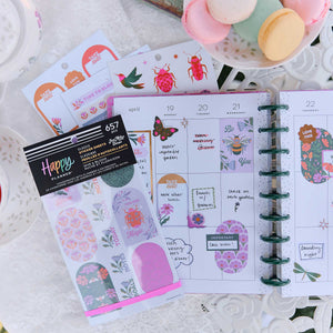 Hive & Bloom sticker book beside a weekly planner decorated with flowers and handwritten plans